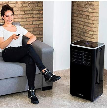 Woman using remote control with portable air conditioner in stylish black design in modern living room.