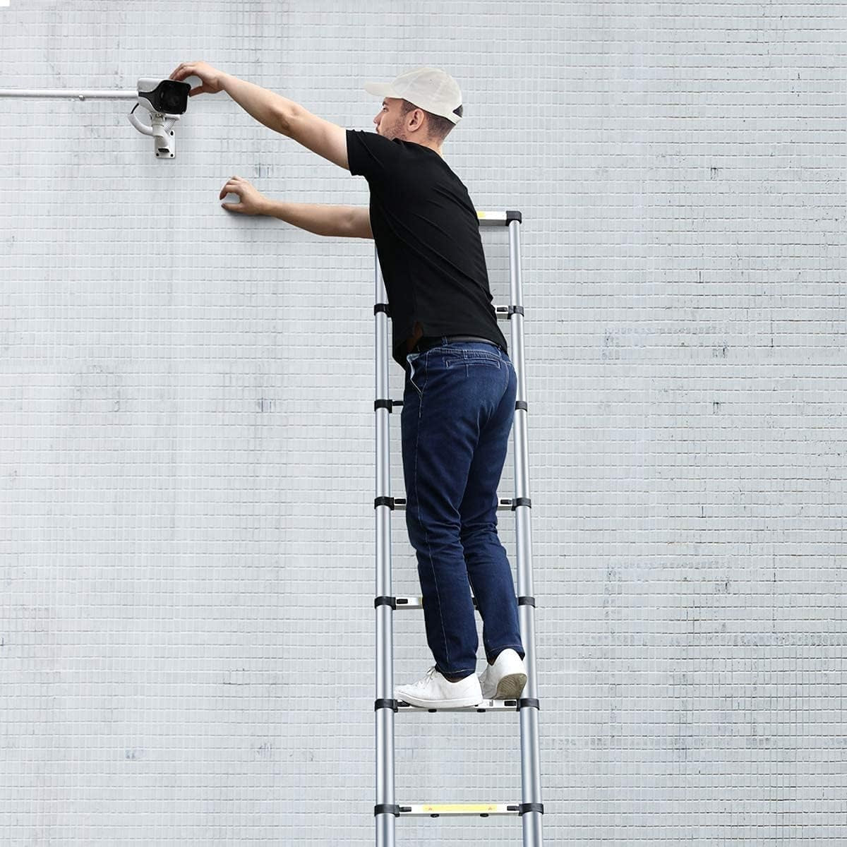 Man using a telescopic aluminum ladder to install a security camera on a wall.