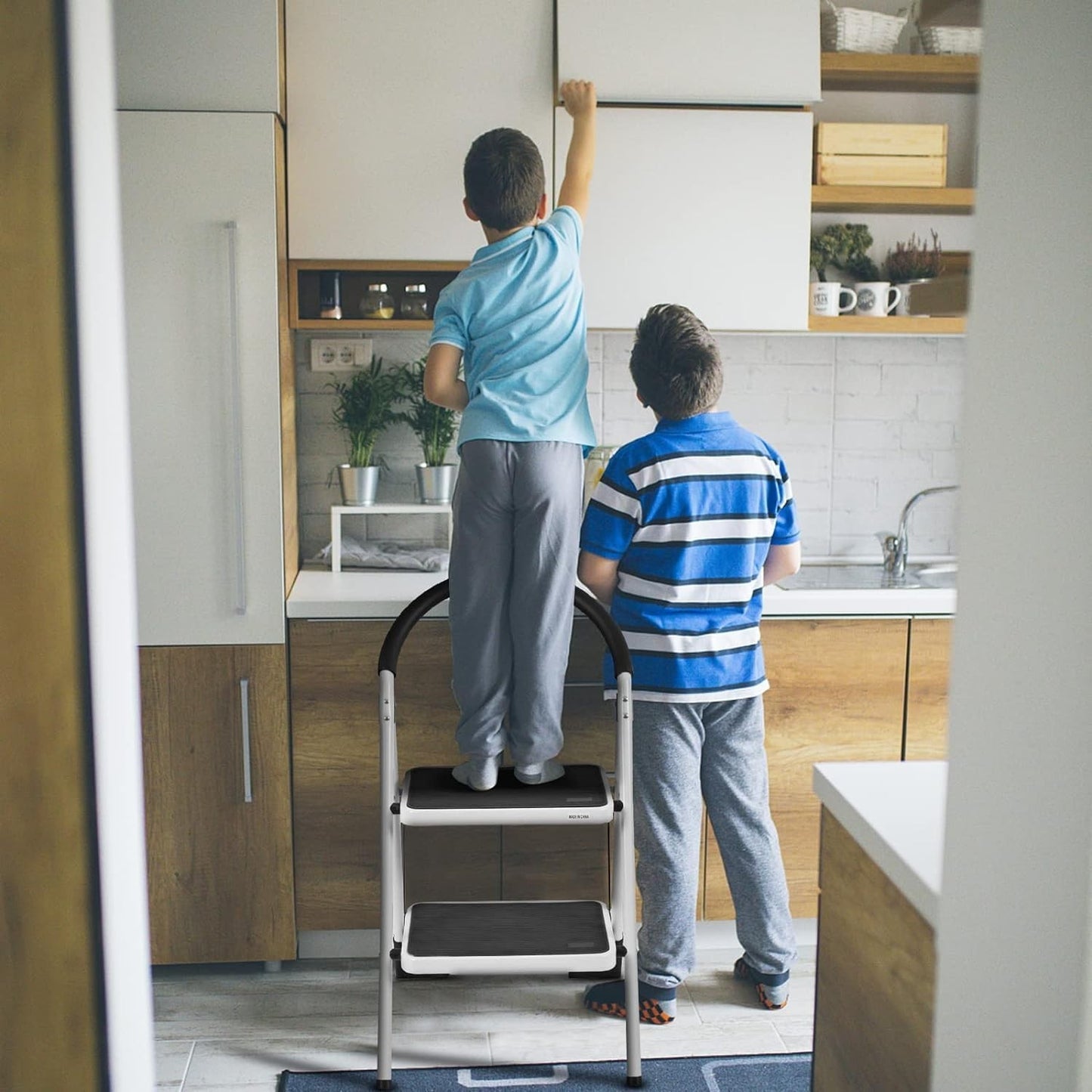 Two children using a foldable step ladder in a modern kitchen, reaching for items on a high shelf.